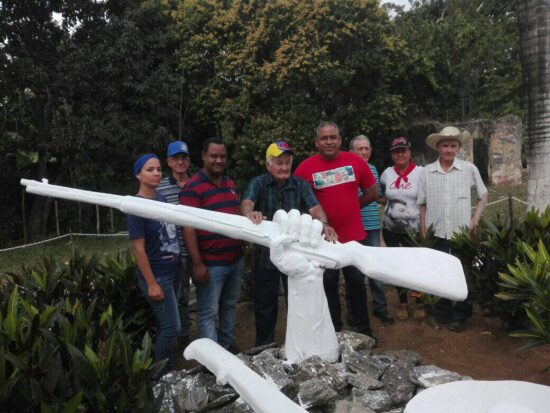 Julio del Sol, sobreviviente de la heroica defensa de Polo Viejo, empuña simbólicamente el fusil de la escultura, junto a dirigentes del municipio de Trinidad. Foto: Alipio Martínez Romero/Radio Trinidad Digital.